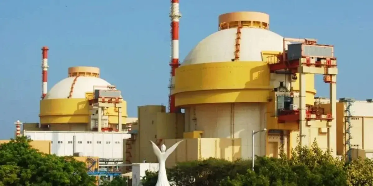 Two domed reactor buildings in yellow and white at Kudankulam, with red-and-white stacks against a blue sky